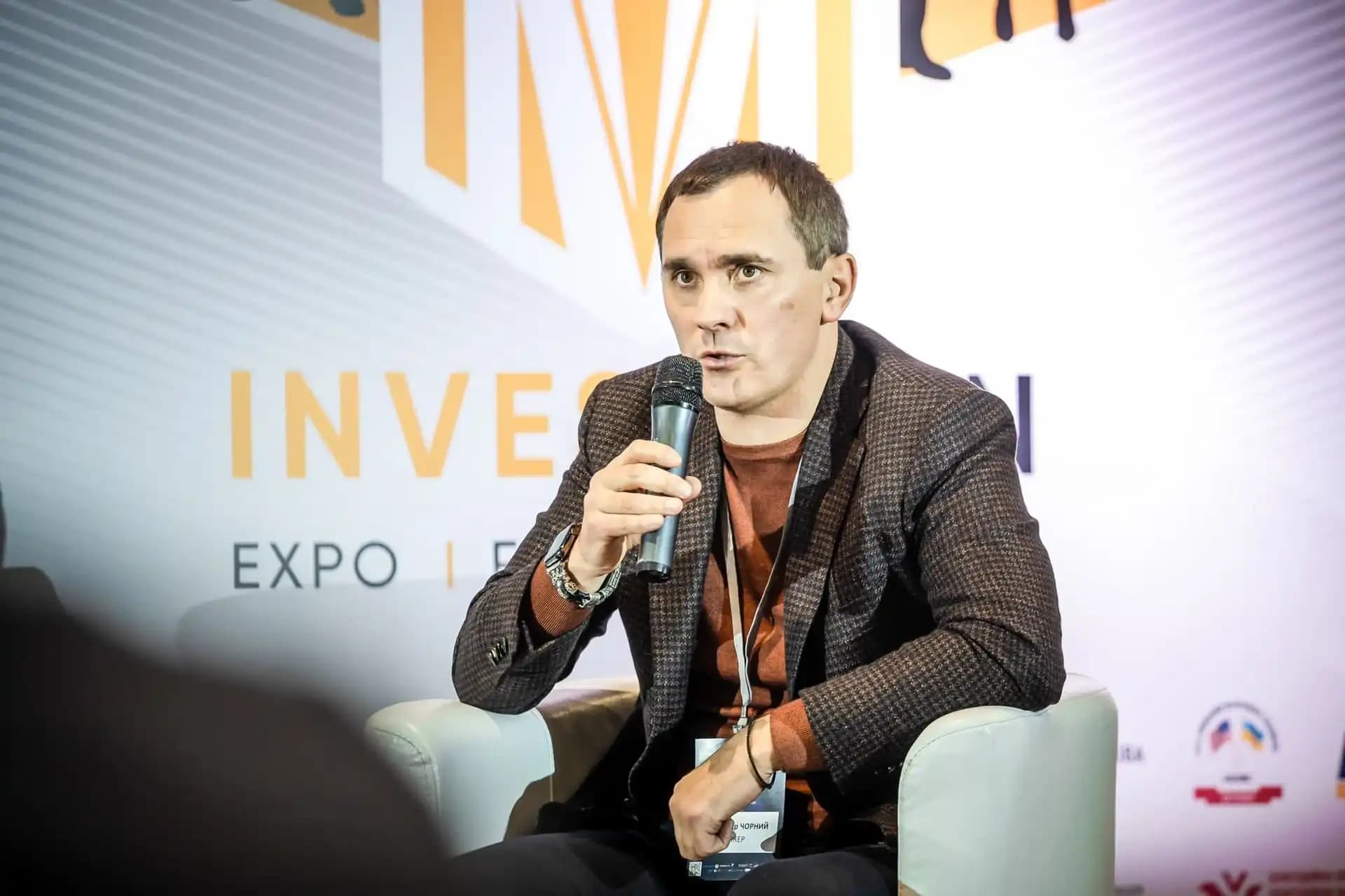 Person speaking into a microphone while seated at an investment expo event.