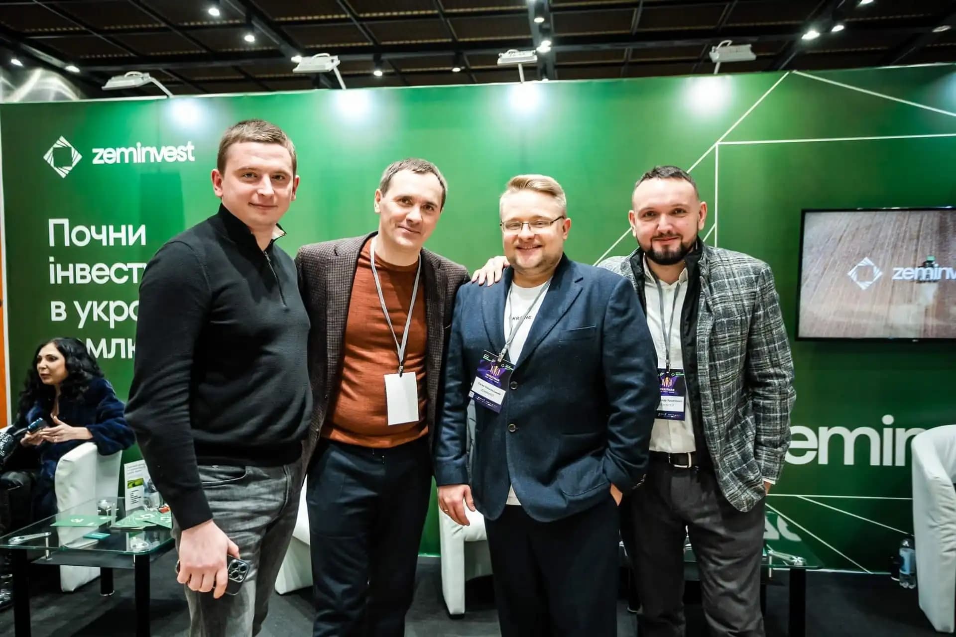 Group of four people posing in front of a green "zeminvest" backdrop at an event.