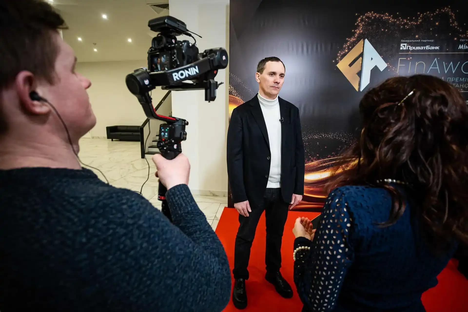 Man being interviewed on a red carpet with a professional camera and FinAwards backdrop.