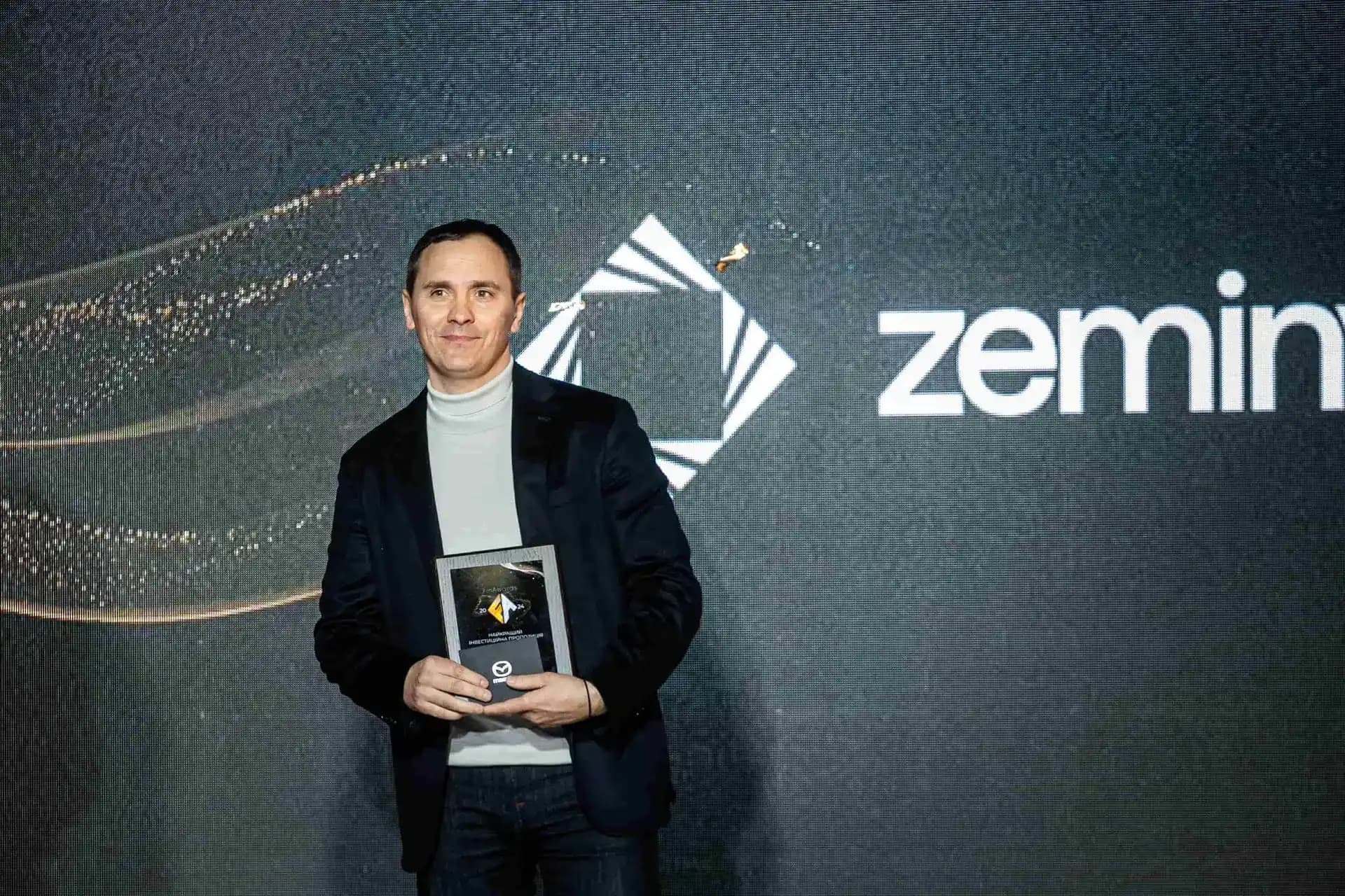 Man holding an award plaque in front of a digital backdrop featuring the Zeminvest logo.