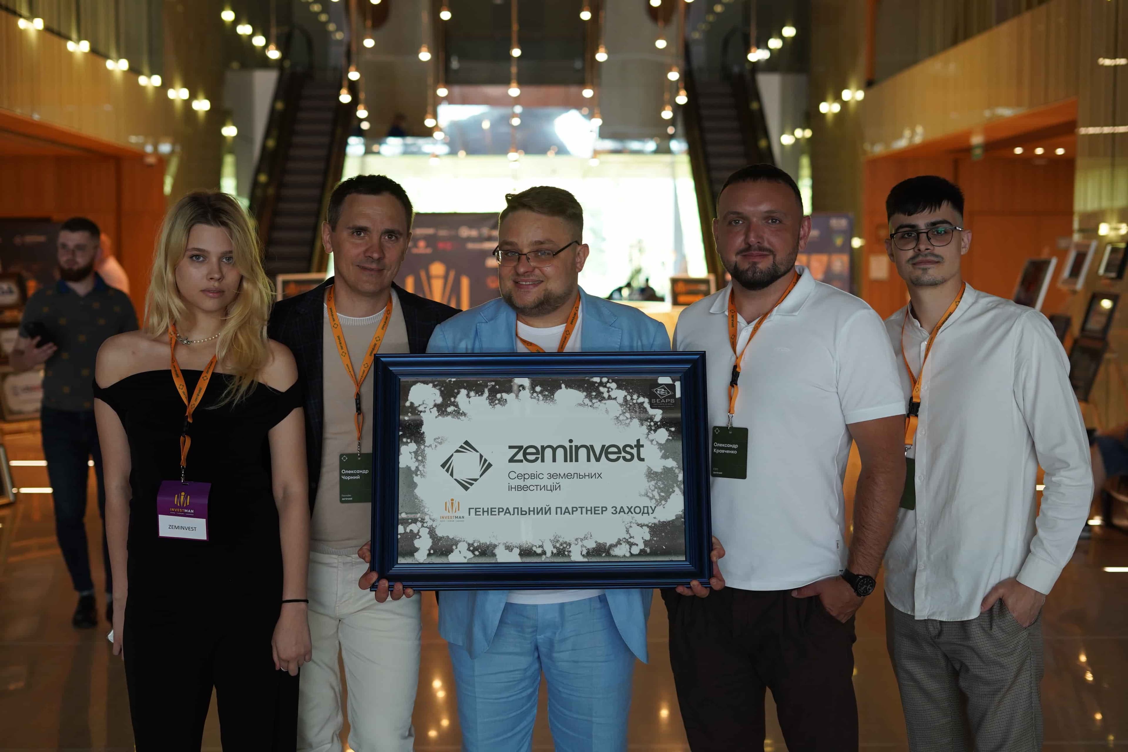 Group holding a framed "zeminvest" sign, standing in a well-lit lobby.