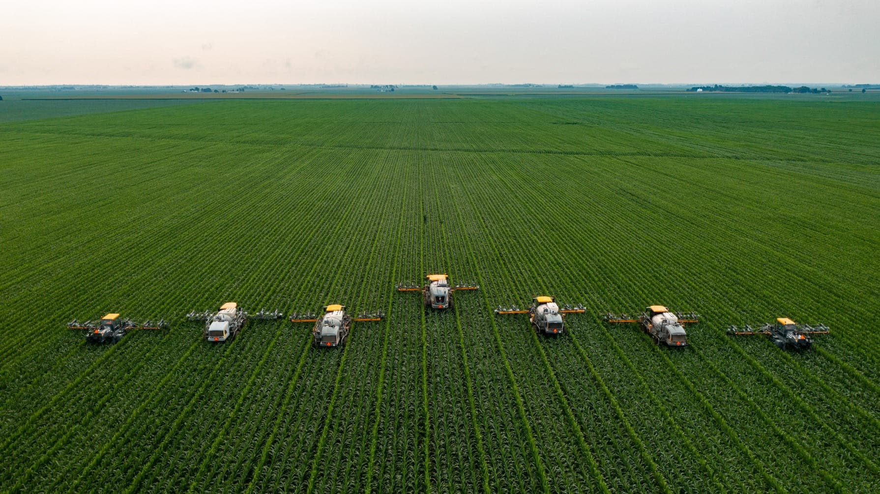 Aerial view of agricultural machinery working in a large, green field.